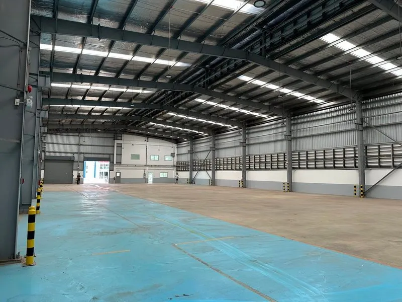 Large empty warehouse interior with high ceilings, skylights, and concrete flooring.