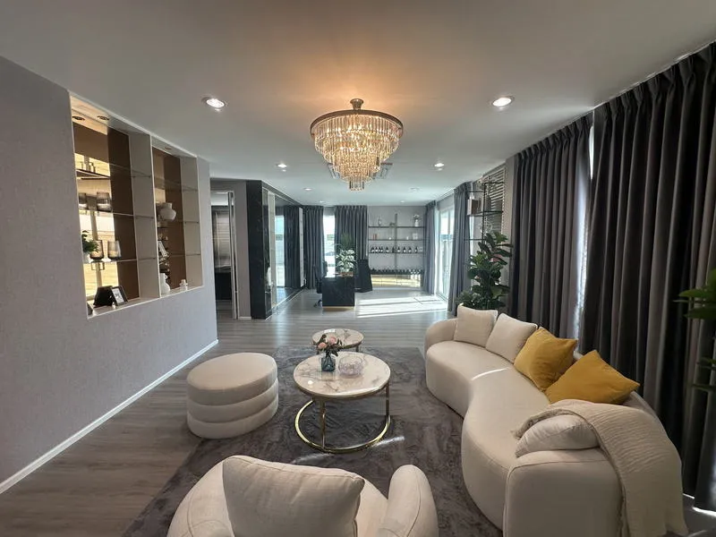 Modern living room with a chandelier, curved sofa, round coffee table, and large windows with curtains.