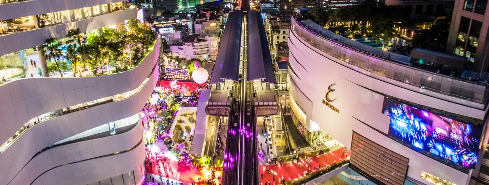 ภาพถ่ายทางอากาศของทิวทัศน์เมืองยามค่ำคืนที่คึกคัก มีอาคารสว่างไสวและชานชาลาสถานีรถไฟ