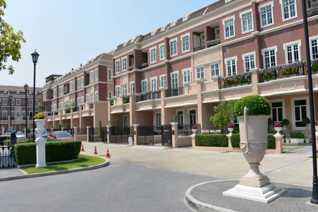 Exterior view of a modern multi-story residential building with brick façade, large windows, balconies, greenery, and a well-maintained driveway.