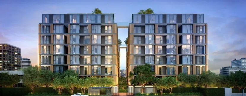 Modern residential building with large glass windows, surrounded by greenery and set against a twilight sky.
