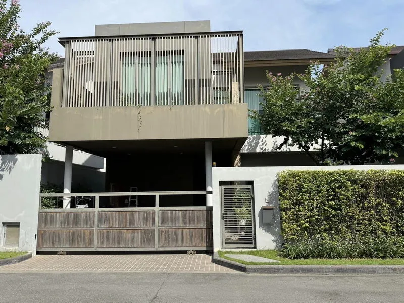 Modern two-story house with wooden gate, vertical slats, and lush greenery.