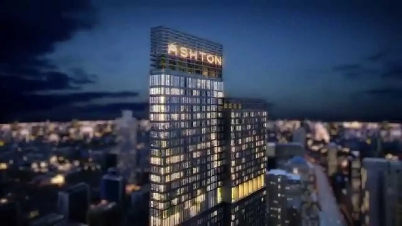 A skyscraper with the word "ASHTON" illuminated at the top, set against a nighttime cityscape.