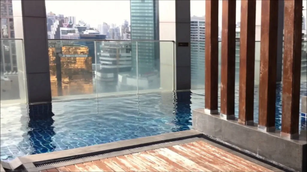 Rooftop infinity pool with cityscape view, featuring tall buildings and reflections on the water.