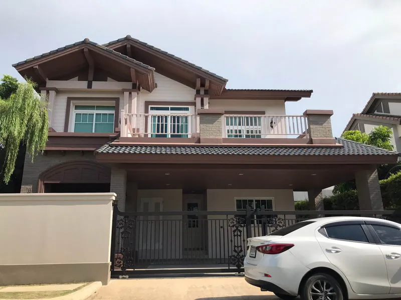 Two-story house with a sloped roof, front balcony, and a white car parked in the driveway.
