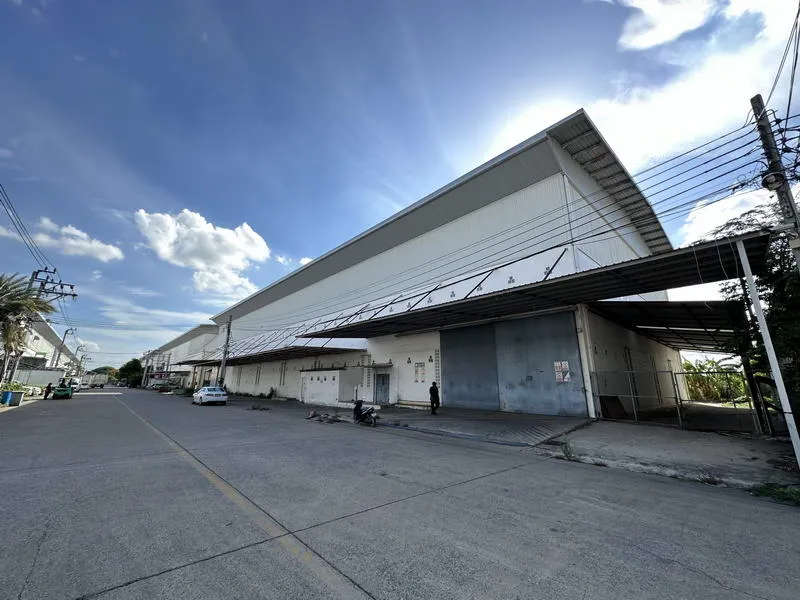 蓝天下，一座大型工业仓库矗立着，宽敞的入口和波纹金属屋顶格外醒目。电线沿着街道延伸。