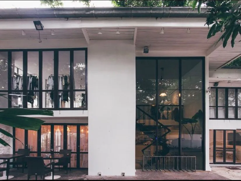 Modern two-story building with large windows, surrounded by greenery; outdoor seating area visible.
