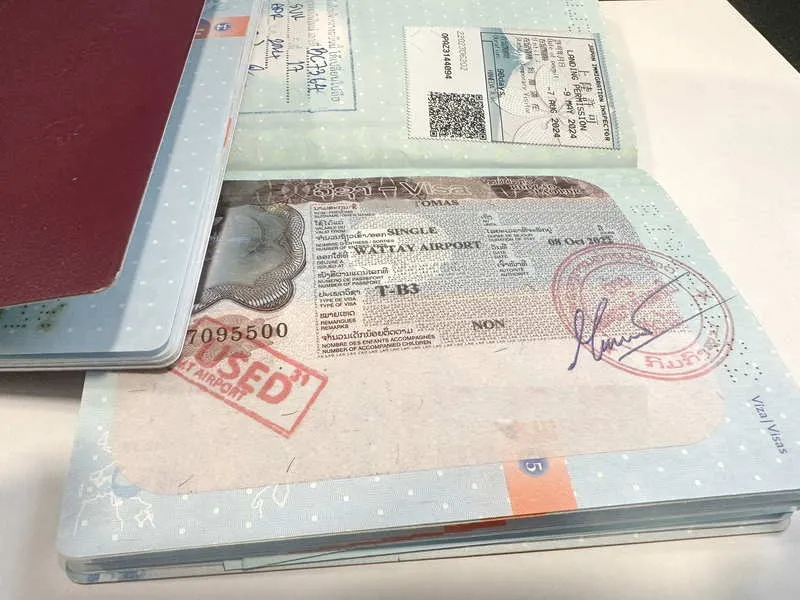 เปิดหนังสือเดินทางที่แสดงวีซ่าไทยที่มีตราประทับ และบัตรโดยสารที่สอดไว้ด้านใน