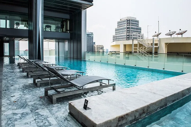 สระว่ายน้ำไร้ขอบบนดาดฟ้า พร้อมเก้าอี้อาบแดด มองเห็นทิวทัศน์เมืองที่เต็มไปด้วยตึกสูงท