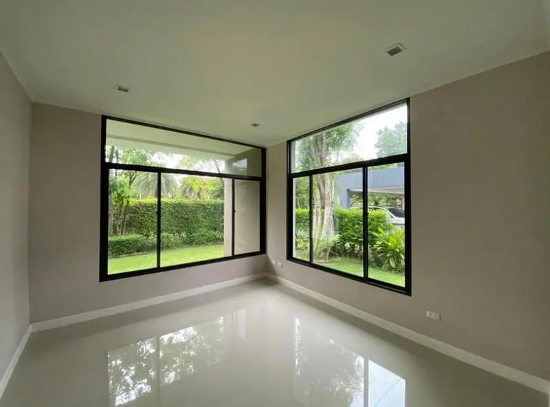 Empty room with large windows overlooking a garden, featuring beige walls and a glossy white floor.