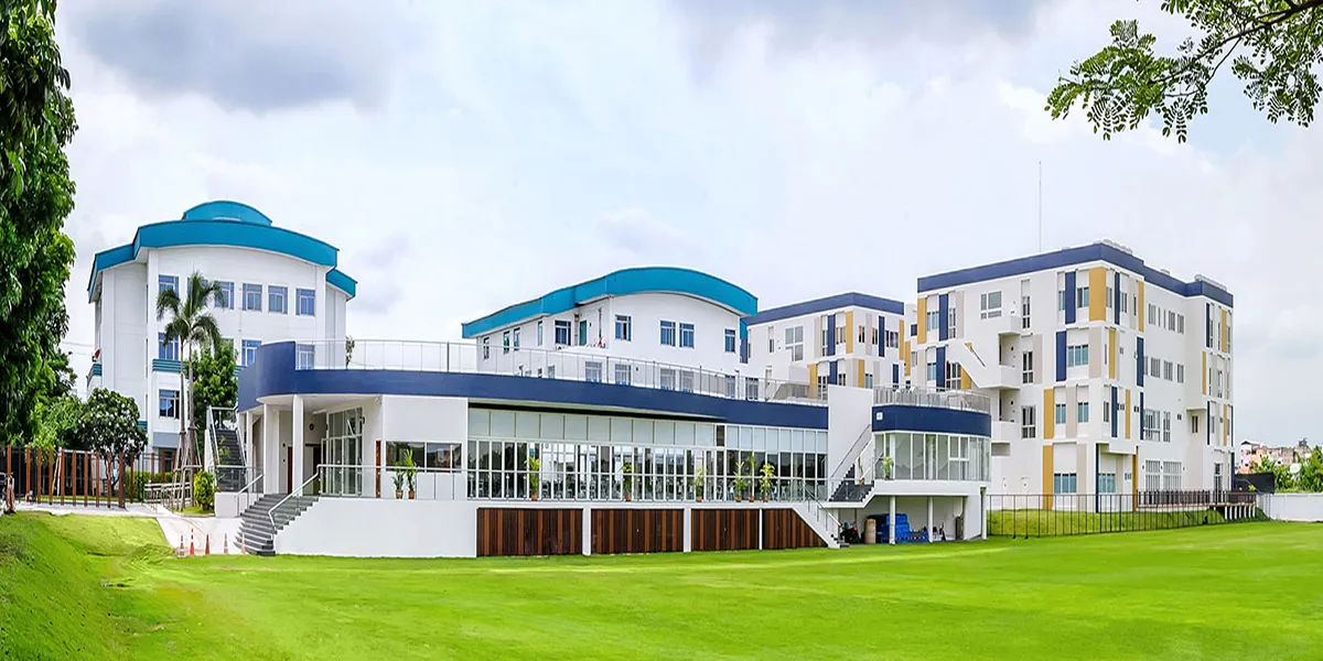 Modern educational building with blue roofs, surrounded by green lawns and trees under a cloudy sky.