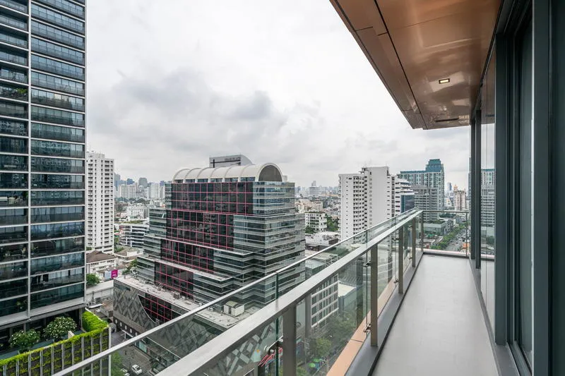High-rise cityscape view from a balcony with glass railing, featuring modern buildings under a cloudy sky.