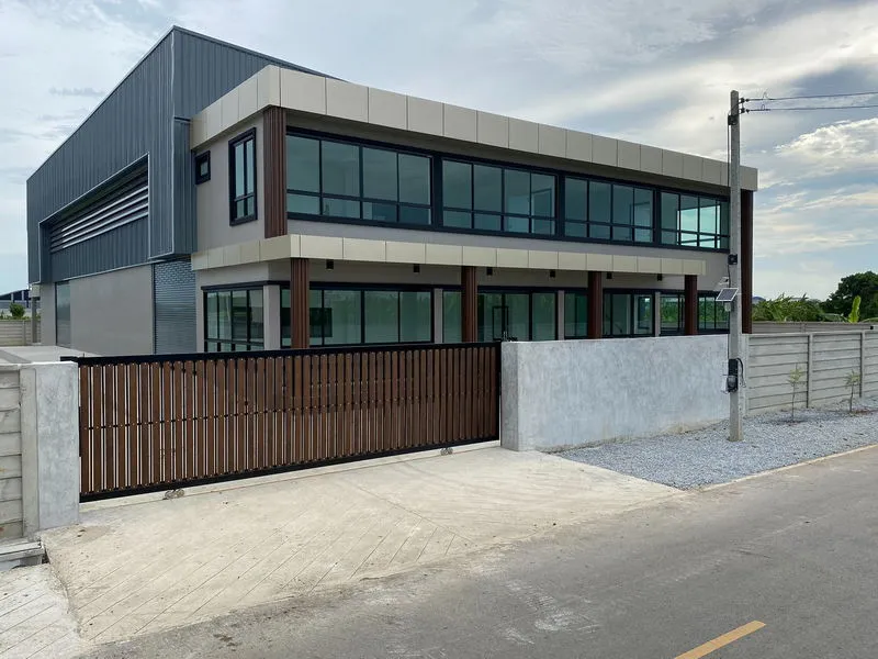 Modern industrial building with large windows and a wooden gate, set against a partly cloudy sky.