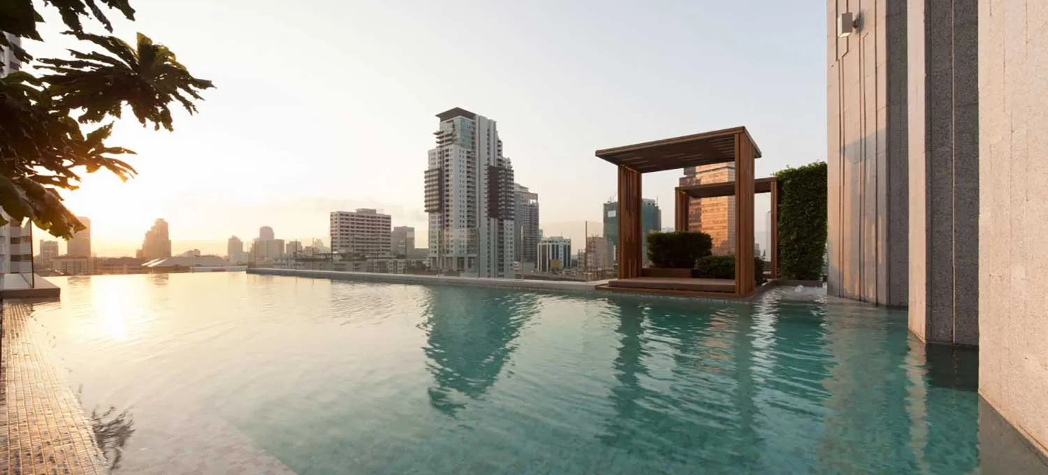 สระว่ายน้ำไร้ขอบบนดาดฟ้า มองเห็นวิวเส้นขอบฟ้าของเมืองยามพระอาทิตย์ตกดิน พร้อมด้วยตึก