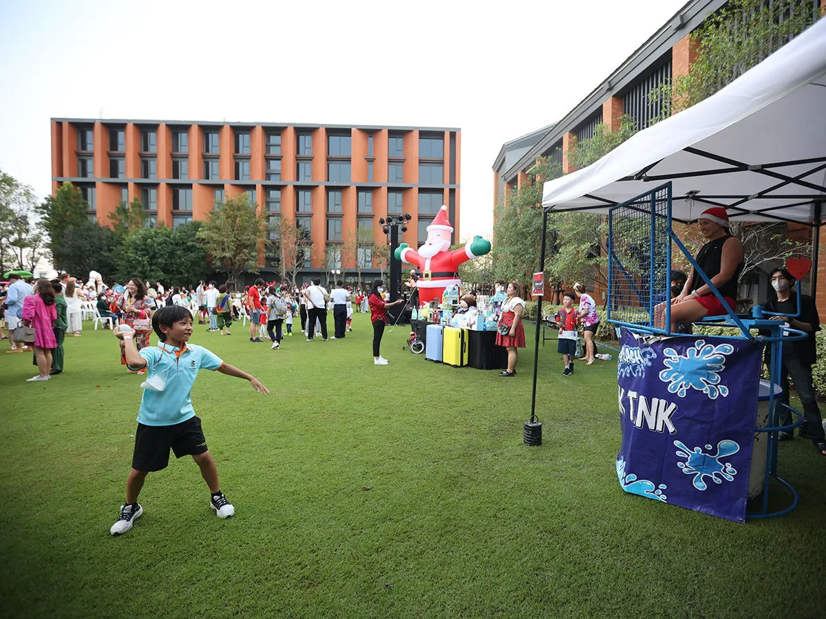 เด็กคนหนึ่งกำลังโยนลูกบอลลงในถังน้ำ ขณะที่ผู้คนมารวมตัวกันบนสนามหญ้าที่มีตุ๊กตาซานตา