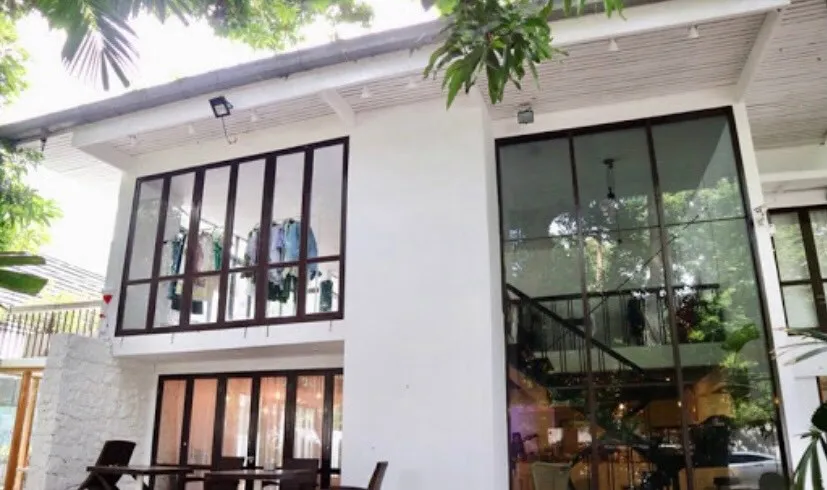 อาคารสองชั้นสไตล์โมเดิร์น มีหน้าต่างบานใหญ่ ล้อมรอบด้วยต้นไม้ ชั้นล่างมีโต๊ะรับประทาน