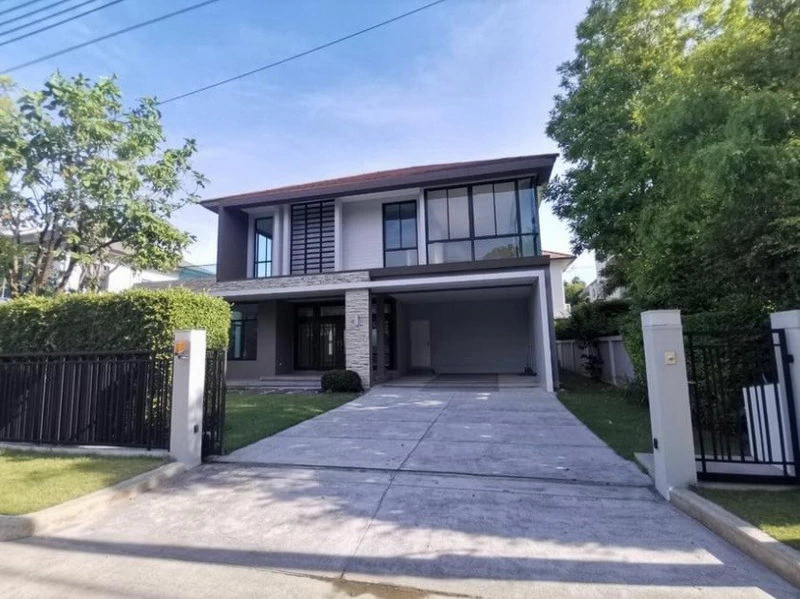 บ้านเดี่ยวสองชั้นสไตล์โมเดิร์น พร้อมทางเข้าจอดรถ โรงจอดรถ และต้นไม้เขียวขจีโดยรอบ ในวั