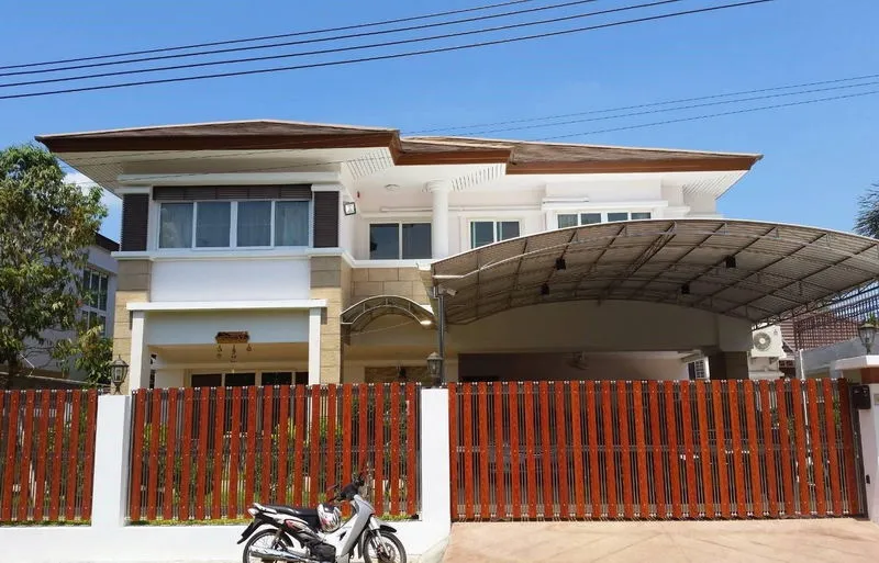 article image - Two-story house with a brown roof, metal carport, red fence, and parked motorcycle in the driveway. Two-story house with a brown roof, metal carport, red fence, and parked motorcycle in the driveway.