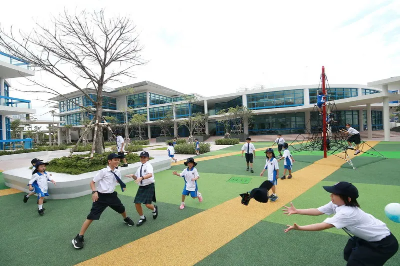 Children playing on a colorful playground outside a modern school building.