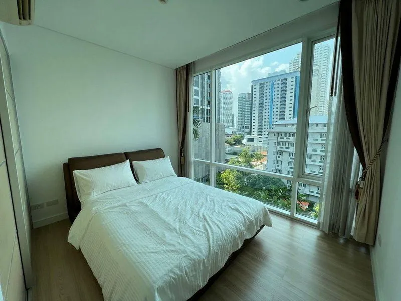 Bright bedroom with a large bed, white linens, and floor-to-ceiling windows offering a city view.