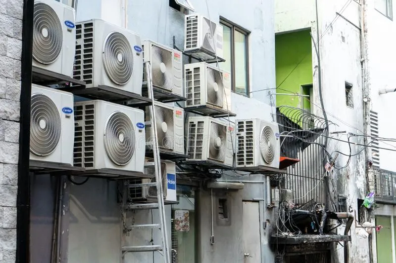 Multiple air conditioning units mounted on the exterior wall of an urban building with visible wiring.