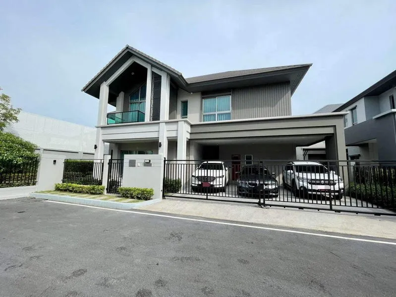 Modern two-story house with a gated driveway, three parked cars, and a neat front yard on a clear day.