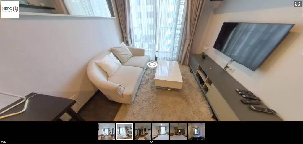 Modern living room with a white sofa, coffee table, wall-mounted TV, and floor-to-ceiling window with curtains. Cozy rug and decor accents complete the space.
