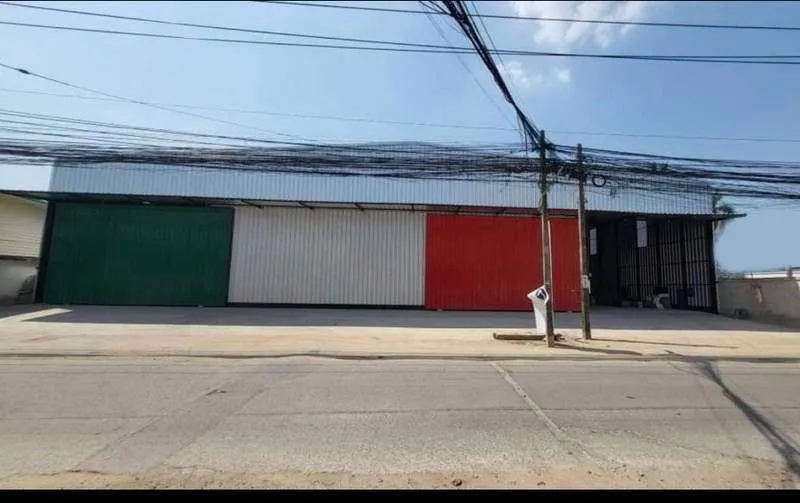Industrial building exterior with a corrugated metal facade featuring green, white, and red sections, power lines overhead, located along an empty street.