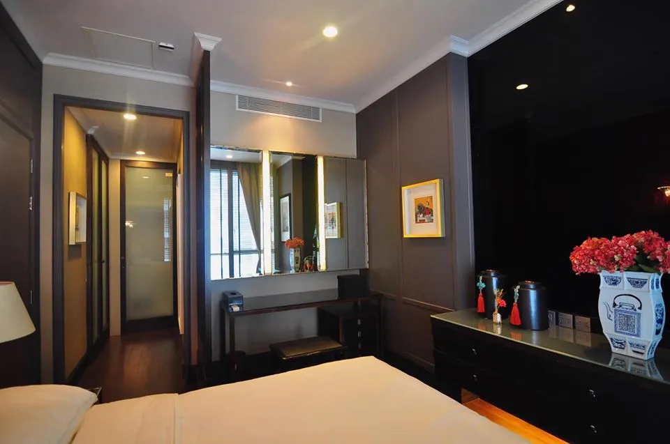 Stylish hotel room with a bed, vanity mirror, floral arrangement, decorative items, and art on the walls.