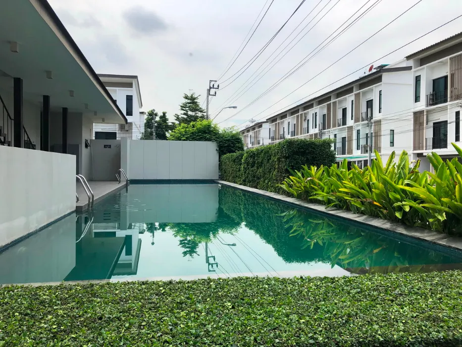 Outdoor swimming pool beside modern residential buildings, with green plants alongside.