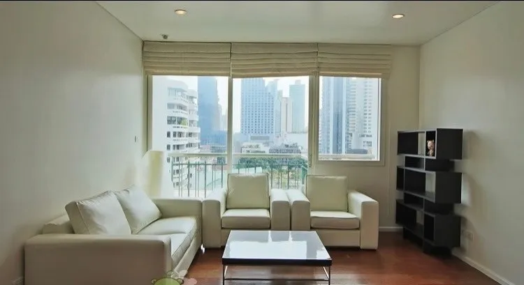 Modern living room with white sofas, a coffee table, and large windows overlooking a cityscape.