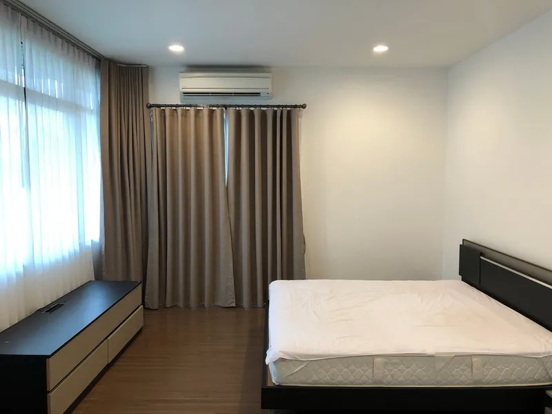 A minimal bedroom with a bed, nightstand, curtains, and an air conditioner.