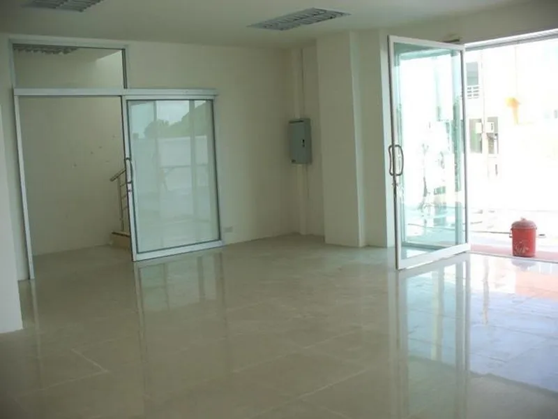 Empty, bright room with tiled floor, glass doors, and a fire extinguisher by the entrance; staircase visible through a door on the left.