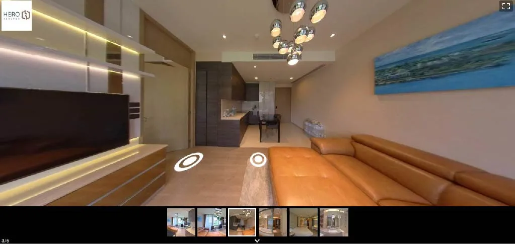 Modern living room with a brown leather sectional sofa, a wall-mounted TV, and a contemporary chandelier. Dining area and kitchen visible in the background.