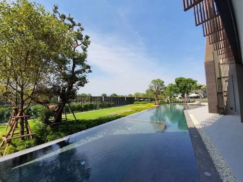 Serene outdoor pool with clear blue water surrounded by trees and a modern building on a sunny day.