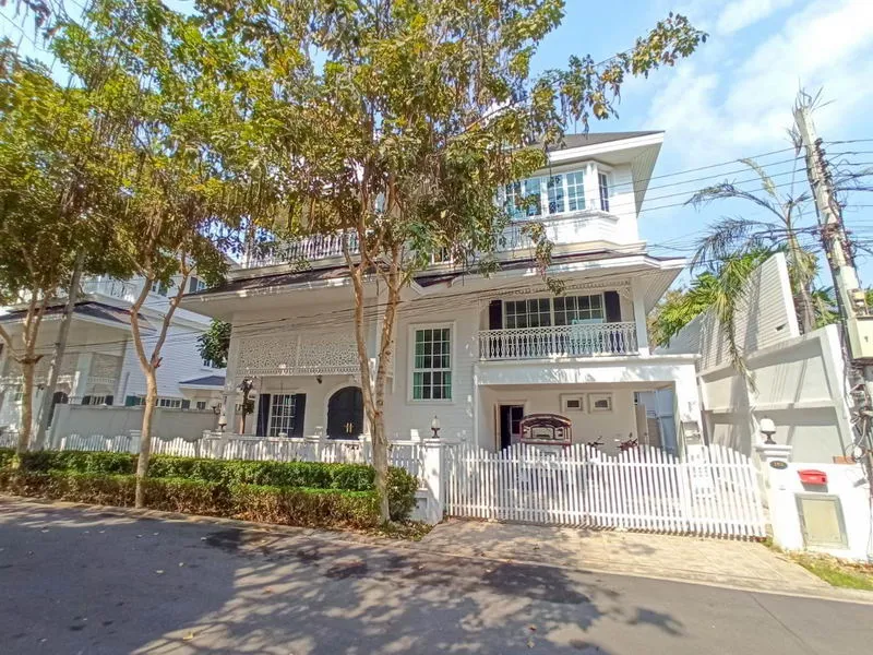 White two-story house with a picket fence and trees in front, under a clear blue sky.