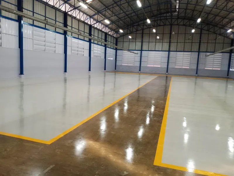 ภายในโกดังว่างเปล่ากว้างขวาง เพดานสูง พื้นคอนกรีต และคานโครงสร้างสีน้ำเงิน