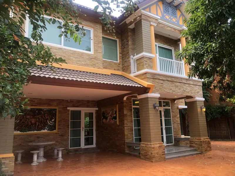 Two-story house with brick exterior, white-framed windows, pillars, and a decorative sheltered entrance, surrounded by trees.