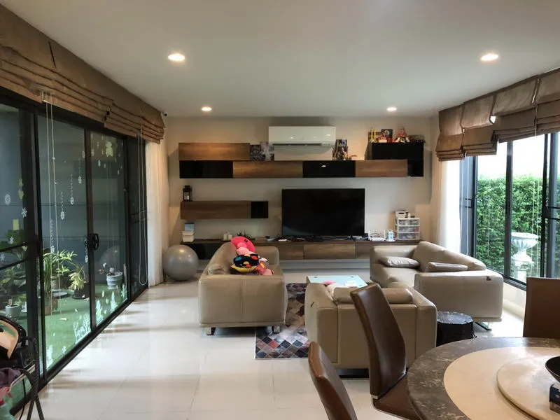 ห้องนั่งเล่นสไตล์โมเดิร์น ตกแต่งด้วยโซฟาสีเบจ โทรทัศน์ ชั้นวางของไม้ และหน้าต่างบานใหญ