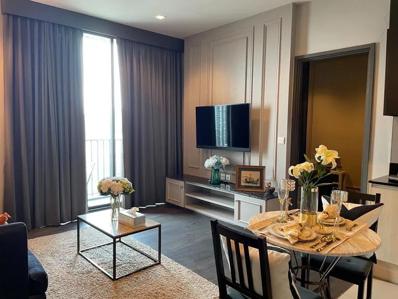 article image - Modern living room with dark curtains, wall-mounted TV, round dining table, elegant decor, and flower arrangements. Modern living room with dark curtains, wall-mounted TV, round dining table, elegant decor, and flower arrangements.