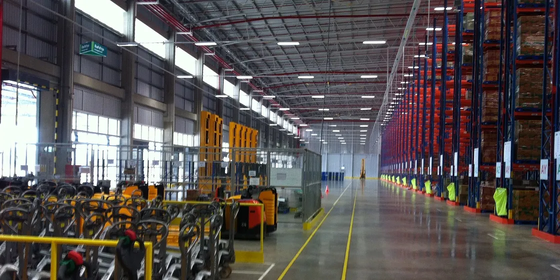 A spacious, well-lit warehouse interior with high ceilings, shelving units, forklifts, and equipment neatly organized along the aisles.