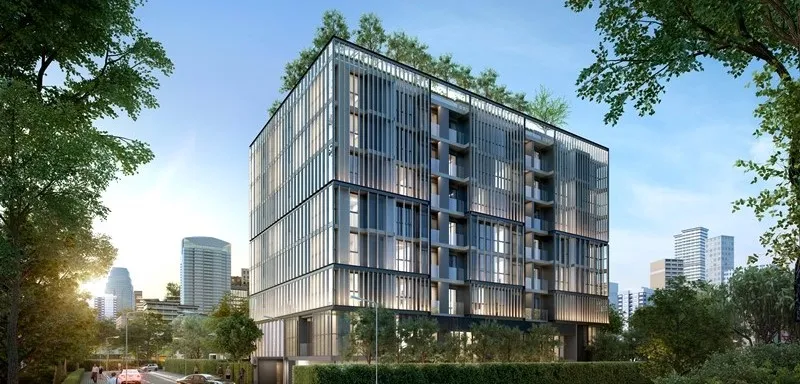Modern multi-story building with glass facade, surrounded by trees and urban skyline in the background, under clear blue sky.