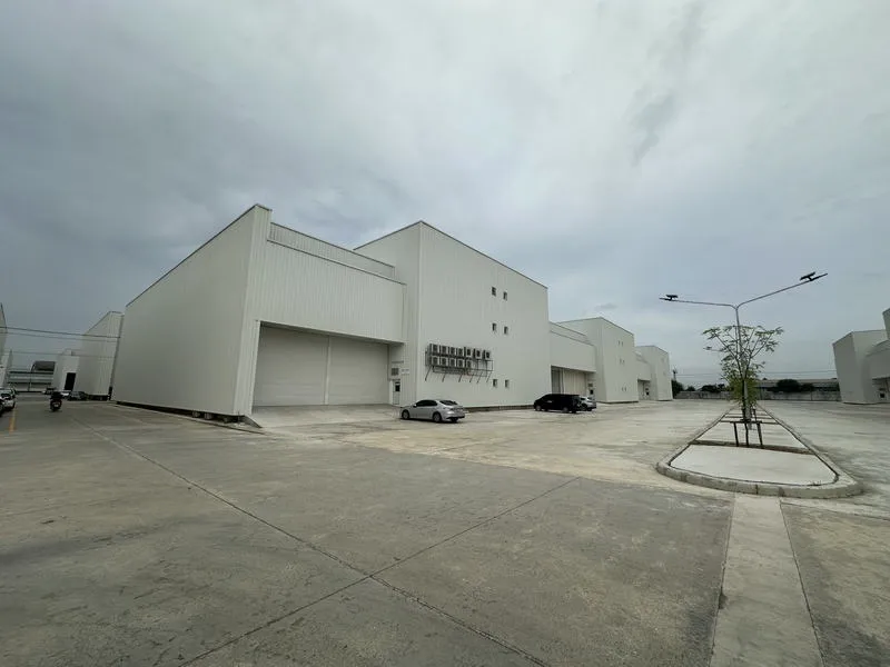 Large industrial warehouses with parked cars and a streetlight under a cloudy sky.