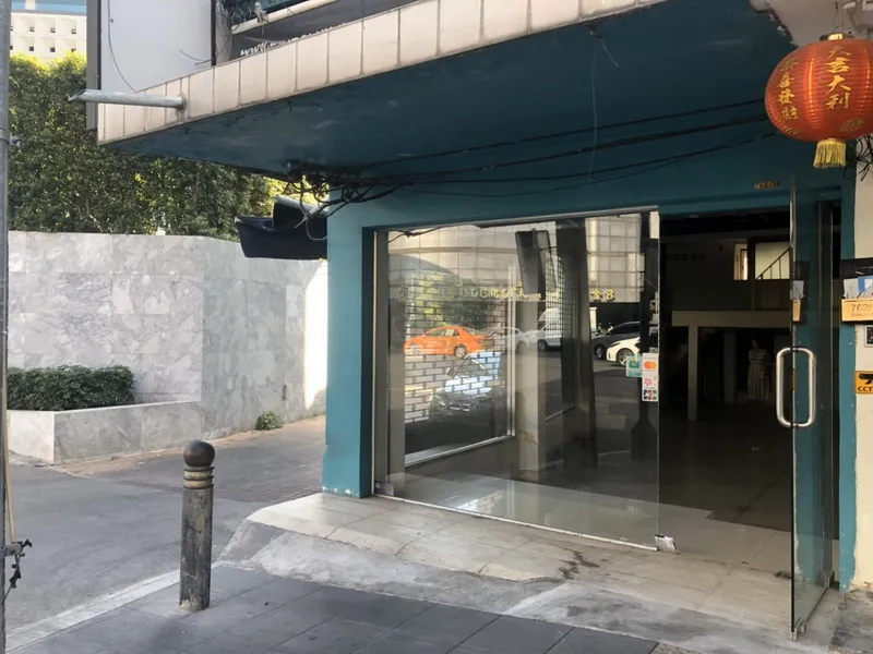Street corner with a teal building and a glass door entrance, a red lantern hanging above, and a marble wall on the side.