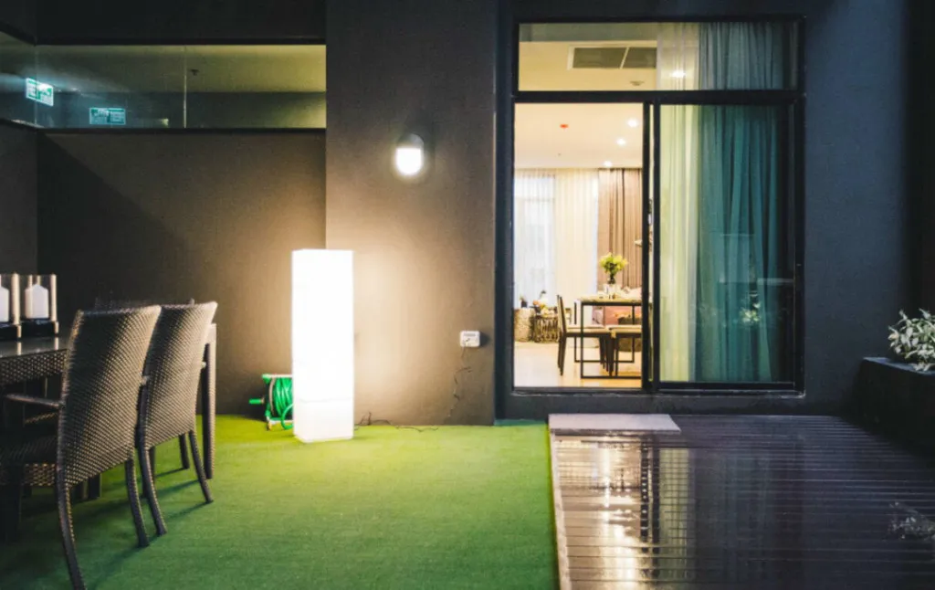 Outdoor patio with dining table, chairs, a lit floor lamp, and sliding glass door leading to an indoor dining area.