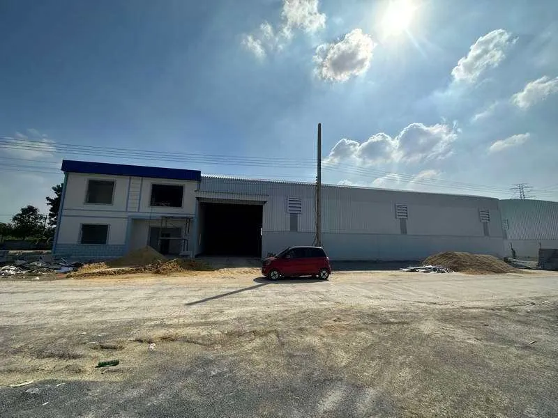 A large industrial warehouse exterior with a red car parked in front under a sunny sky.