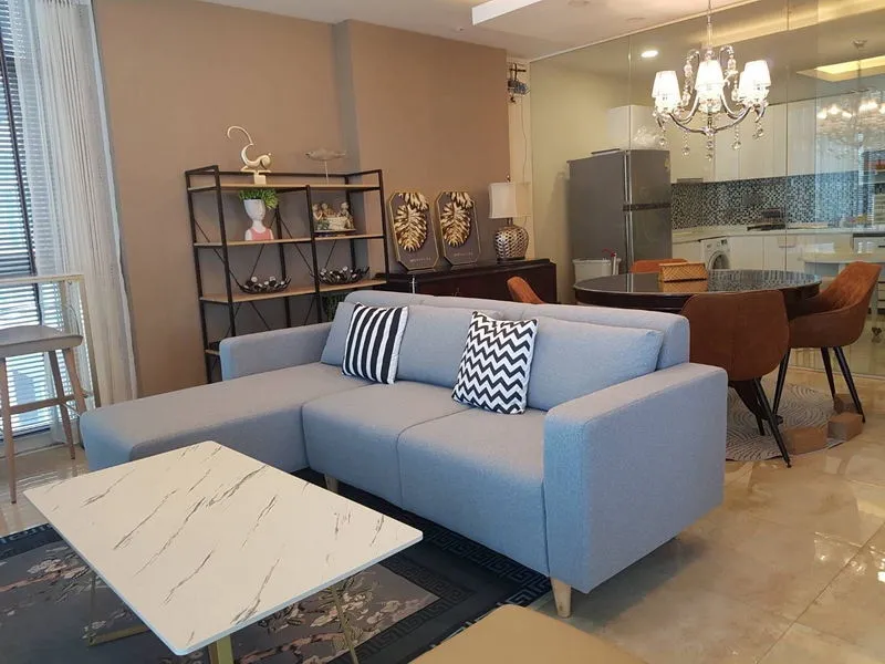 Modern living room with a light blue sofa, striped cushions, marble coffee table, dining area, chandelier, and decorative shelves.