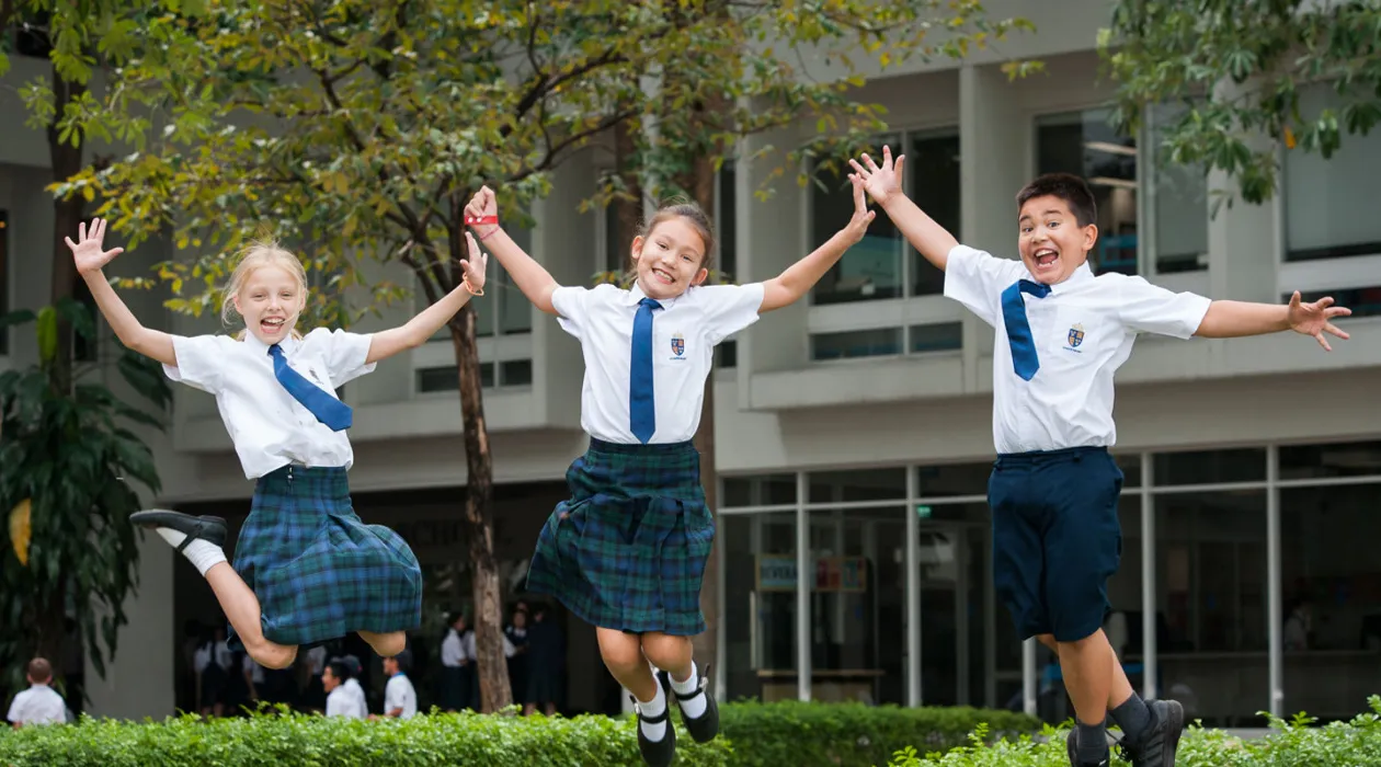 article image - Students in uniform joyfully jumping with arms raised outside a school building. Students in uniform joyfully jumping with arms raised outside a school building.
