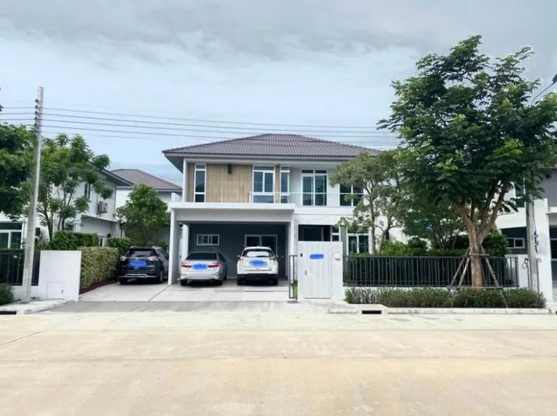 Two-story modern house with a driveway, three cars parked, and trees on both sides, under a cloudy sky.
