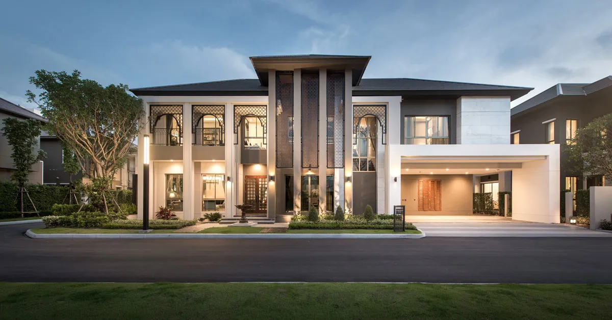 Modern two-story house with large windows, a front garden, and a driveway, set against a clear evening sky.